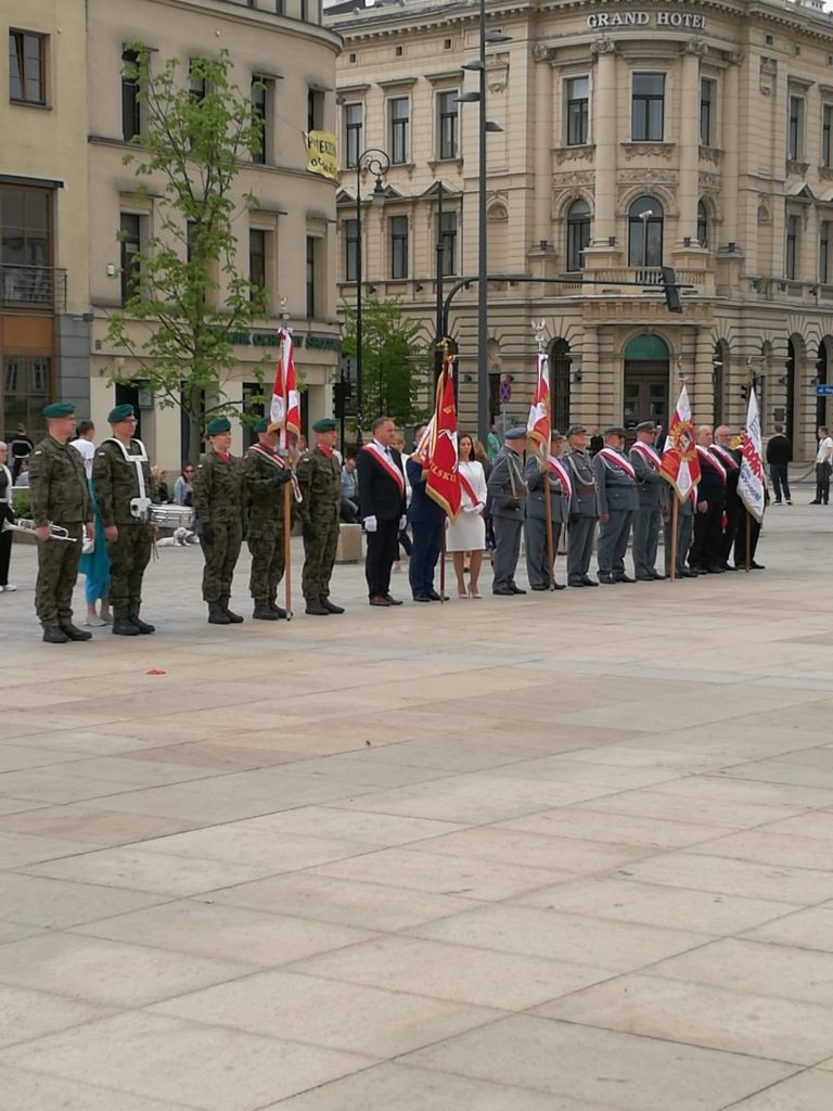 kilkanaście osób na galowo i w mundurach stojących na placu z flagami Polski