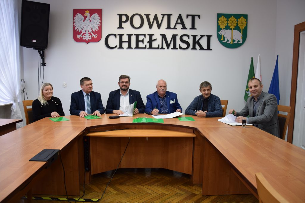 6 osób siedzących przy stole w tle napis "Powiat Chełmski"