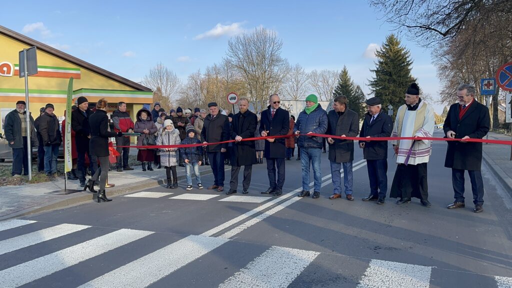 grupa osób stoją na drodze, czerwona wstęga.